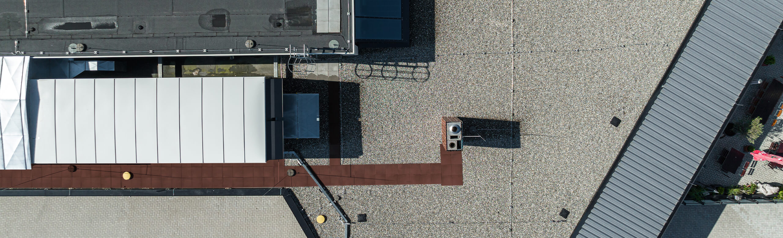 Aerial view of a flat roof with gravel finish, rooftop units and a maintenance walkway; “Construction” text overlay