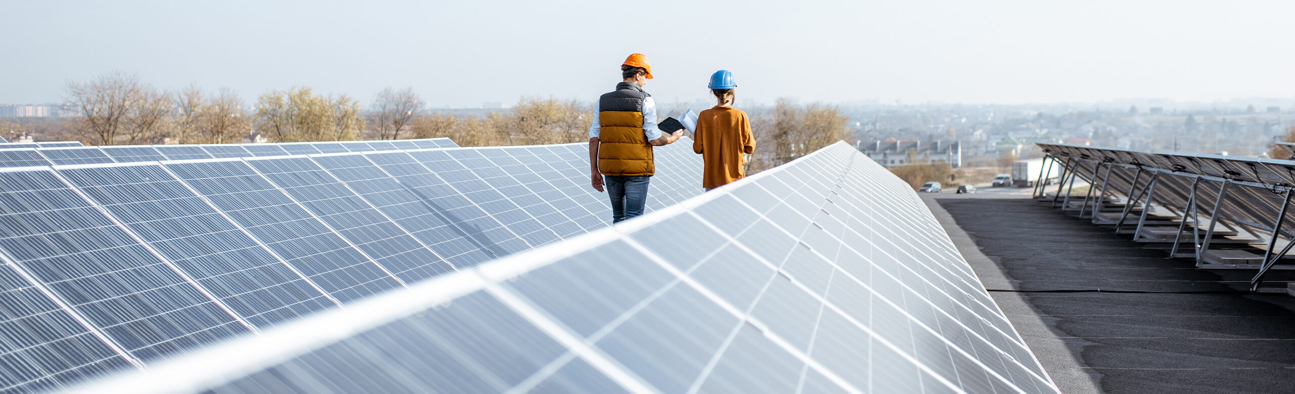 Two helmeted professionals inspecting solar panels on a flat roof; “Construction” text overlay